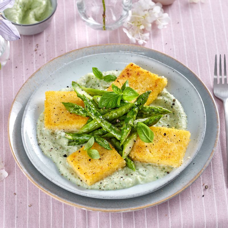 Polentaschnitten mit grünem Spargel, angerichtet auf Kohlrabi-Ricotta-Creme und garniert mit Basilikum.