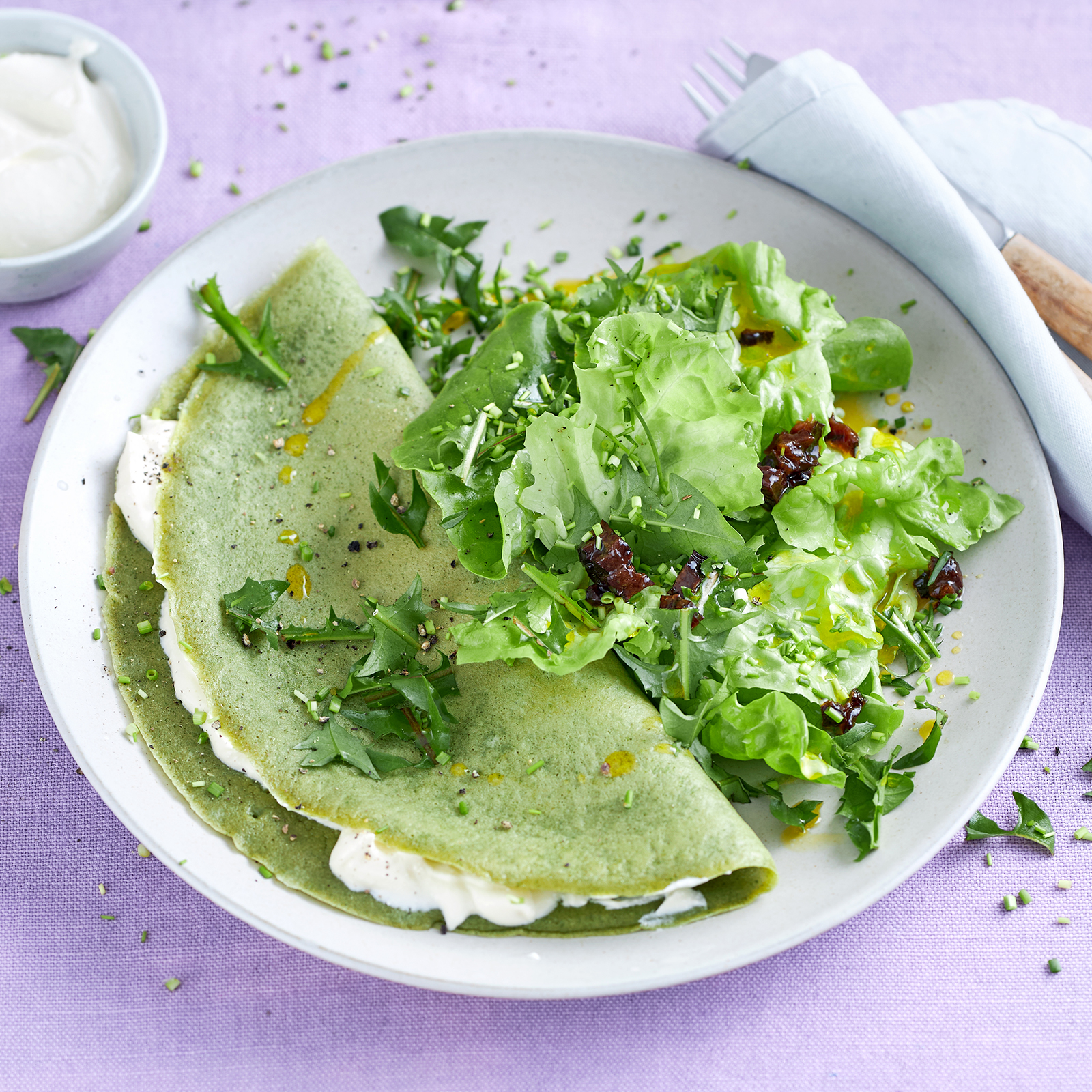 Brennnesselpfannkuchen mit Fetacreme-Füllung, bestreut mit Löwenzahnblättern, dazu ein grüner Salat mit Eichblattsalat und Löwenzahn.