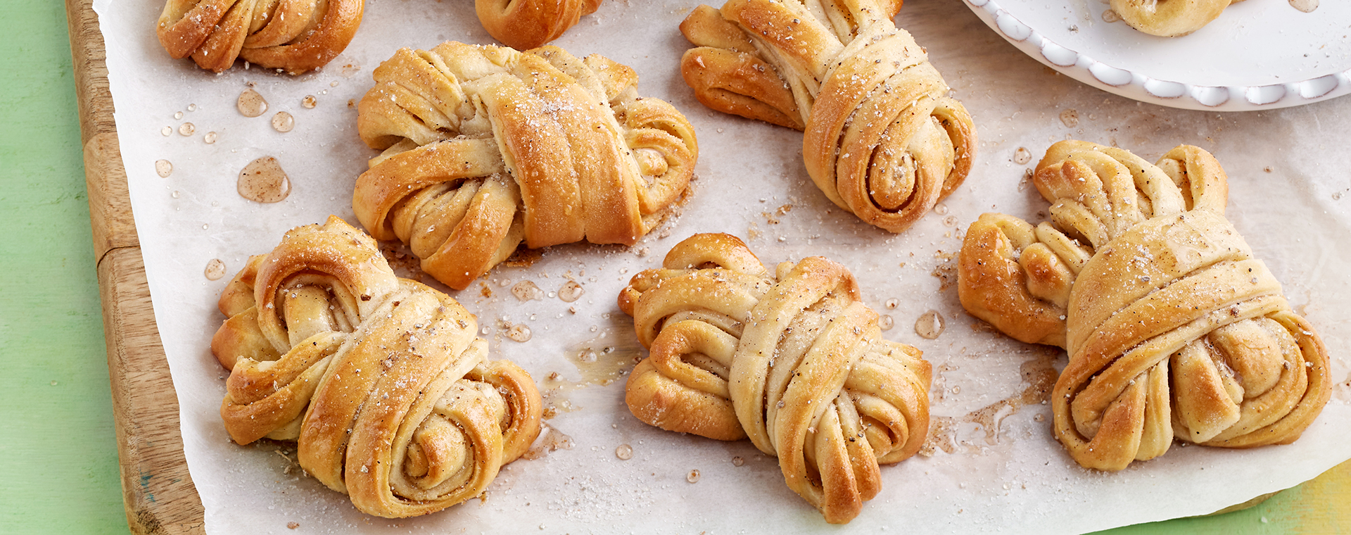 Hefeknoten mit Kardamom auf einem mit Backpapier belegten Brett.