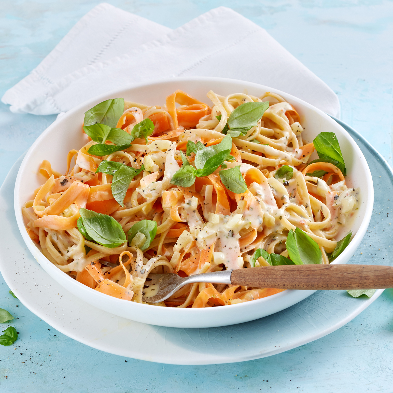 Linguine mit Möhren-Bergkäse-Soße in einer Schale, garniert mit Basilikum.