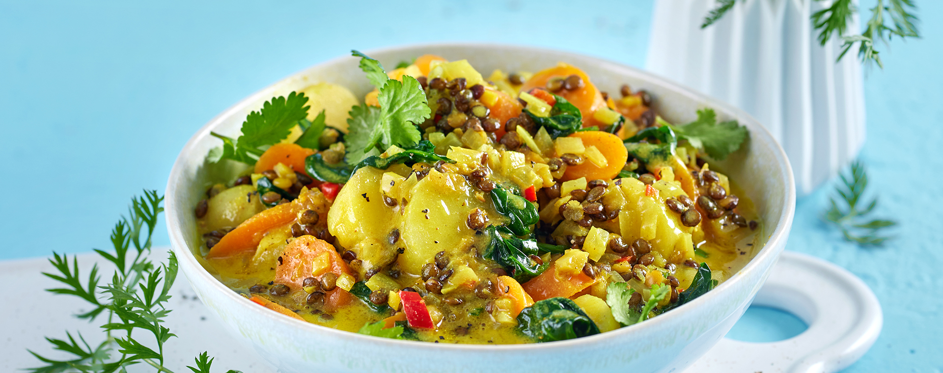 Möhrencurry mit Linsen und Kartoffeln in einer Schale, garniert mit frischem Koriander.