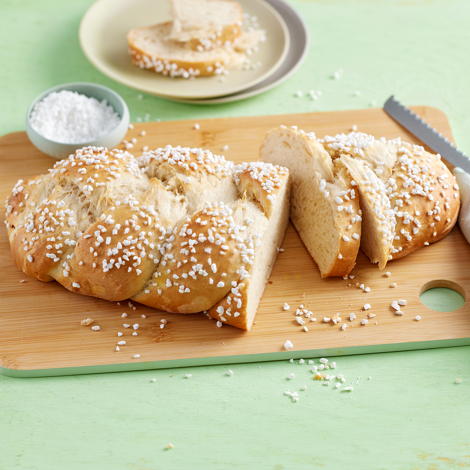 Hefezopf mit Hagelzucker, angeschnitten auf einem Holzbrett.