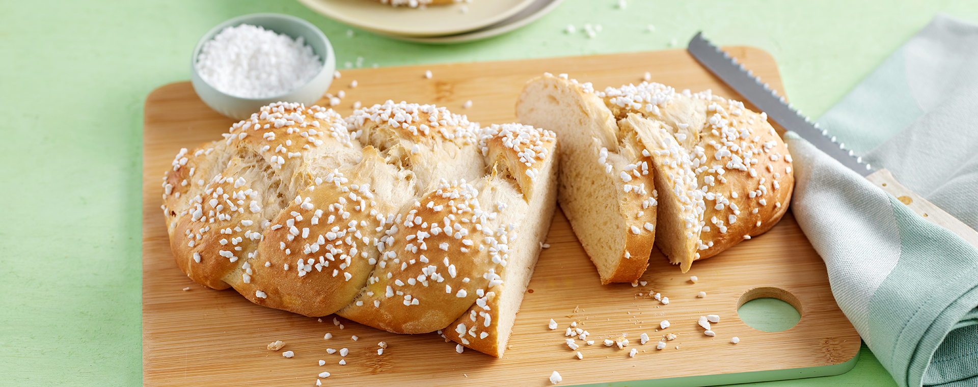 Hefezopf mit Hagelzucker, angeschnitten auf einem Holzbrett.