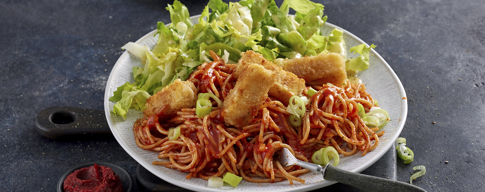 Tomaten-Spaghetti mit Käse-Sticks und Endiviensalat, angerichtet auf einem Teller.